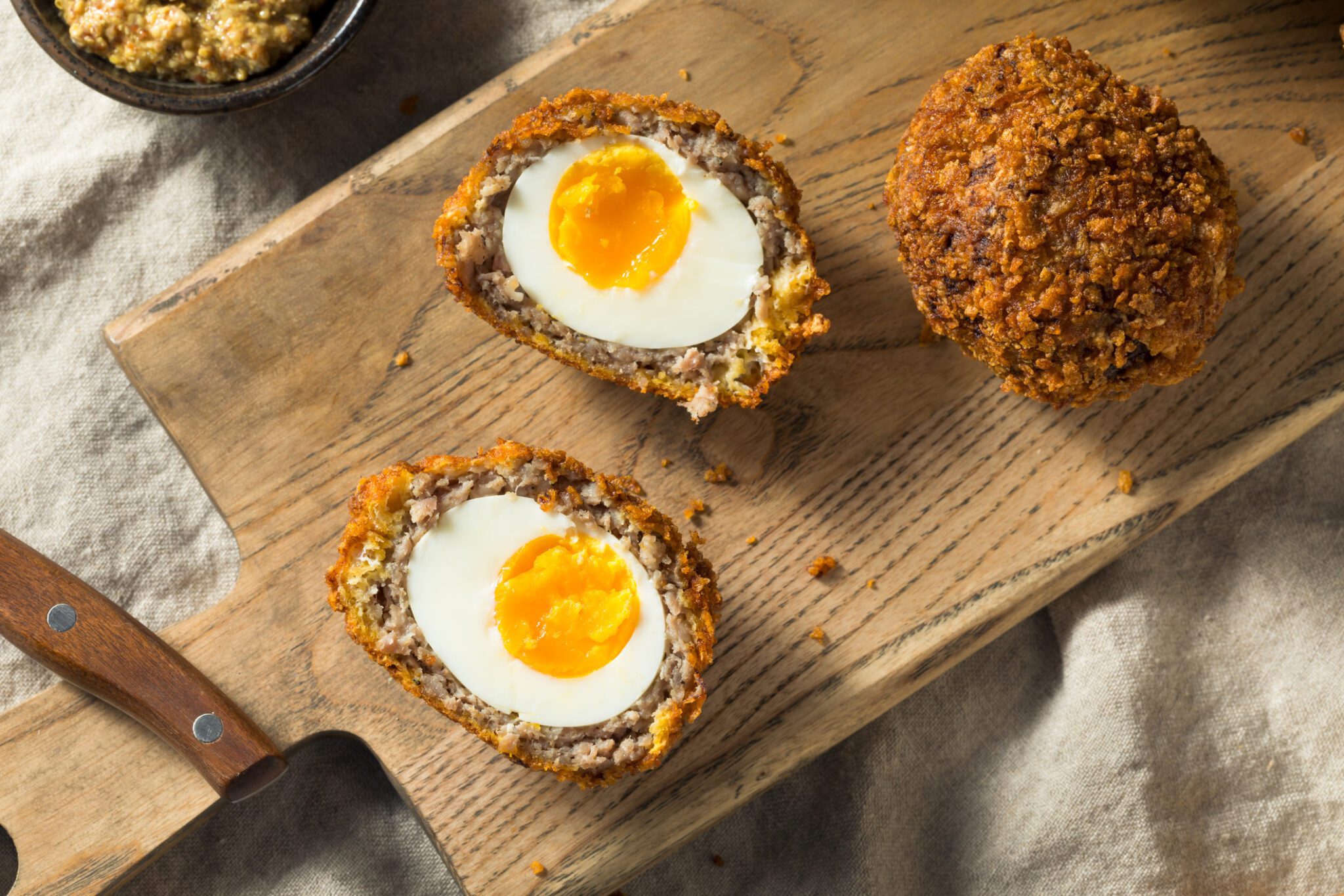 Scotch eggs on a wooden cutting board.